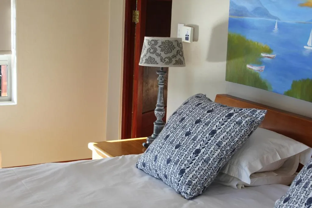 Bright bedroom with wooden bed frame, patterned pillows, and coastal artwork