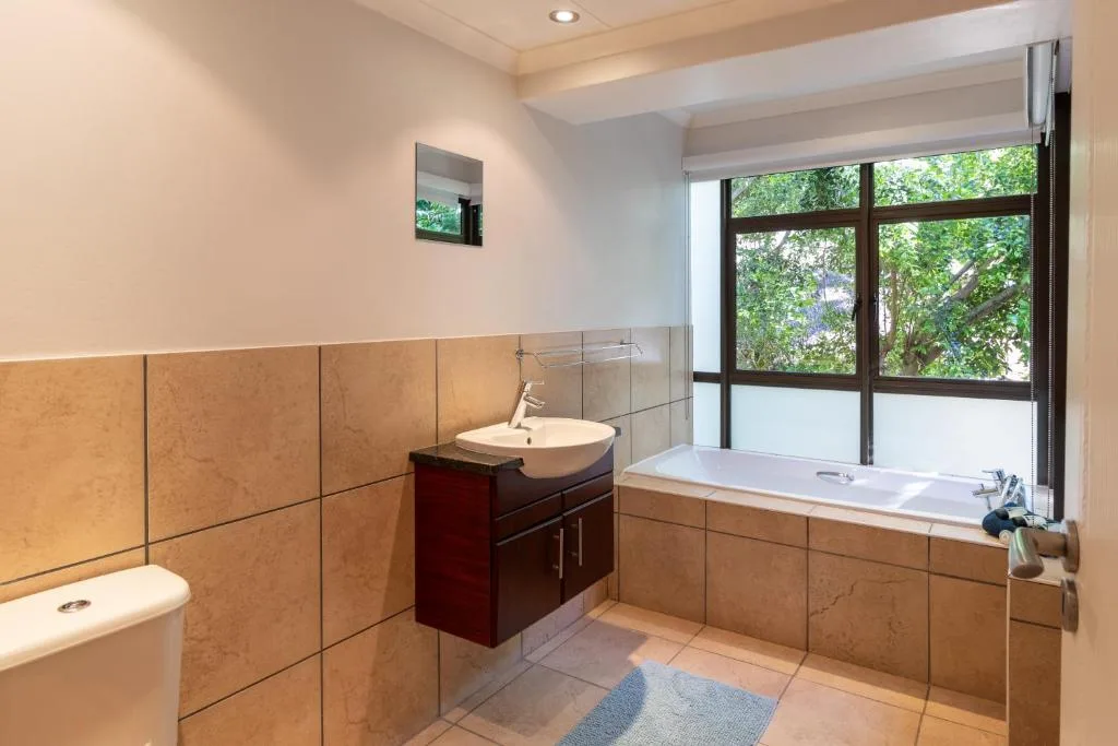 Spacious bathroom with bathtub, vanity sink, and large window overlooking garden