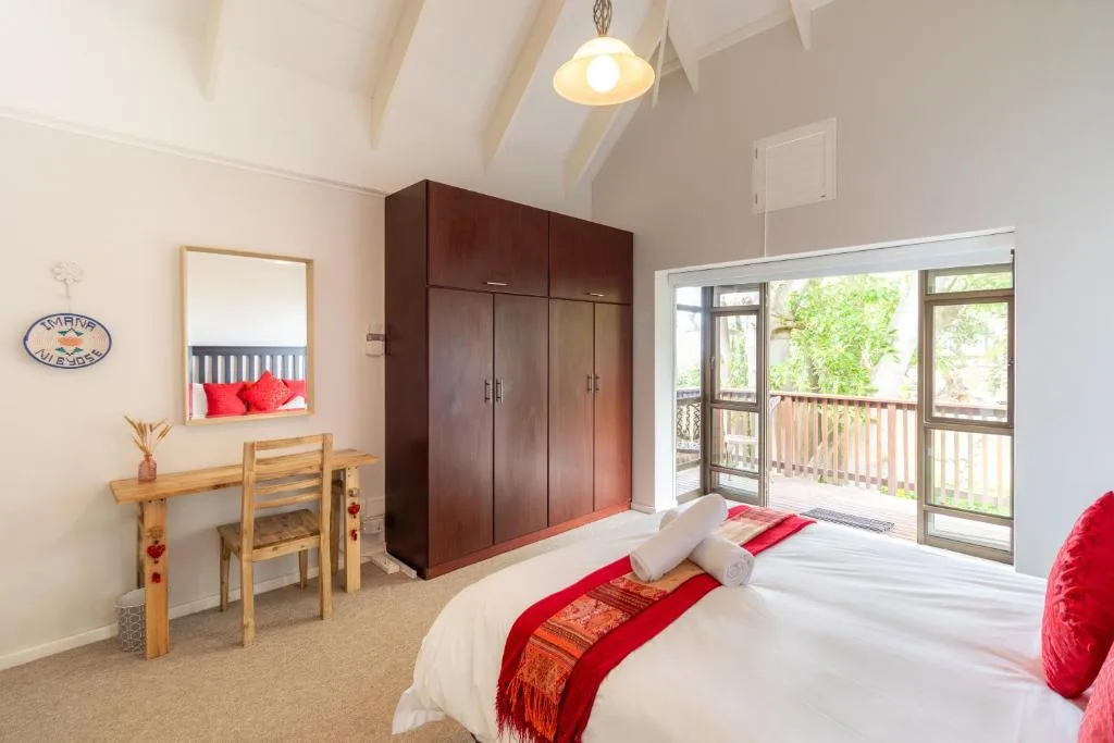 Spacious bedroom with double bed, wooden desk, dark wardrobe, and deck access