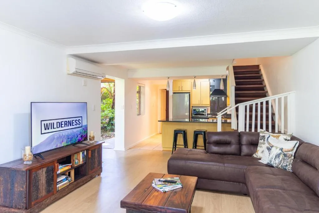 Open-plan lounge with brown leather sofa, TV, and kitchen visible beyond