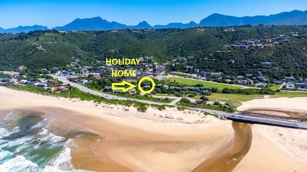 Aerial view of holiday home nestled in lush hills above pristine beach