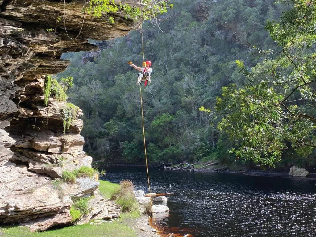Person abseiling from cliff over forested river valley below