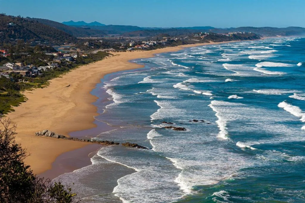 Expansive coastal view of sandy beach with turquoise waves and distant mountains