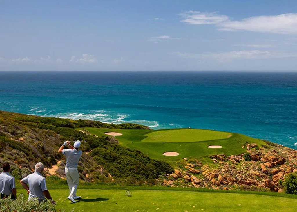 Panoramic ocean and coastline view with golfer on grassy hilltop overlooking turquoise waters