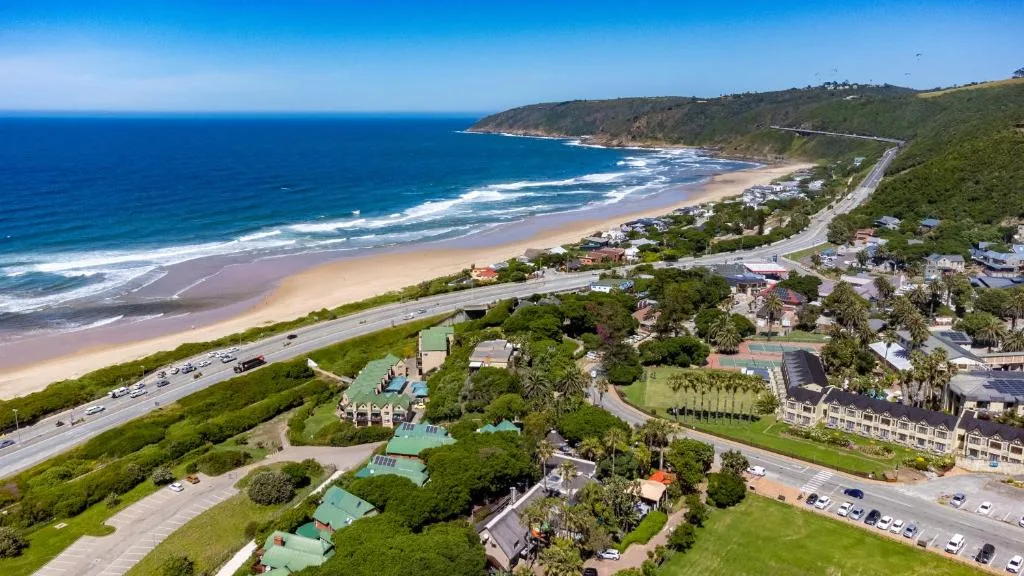 Aerial view of pristine beach, coastal town, and lush green hillside landscape