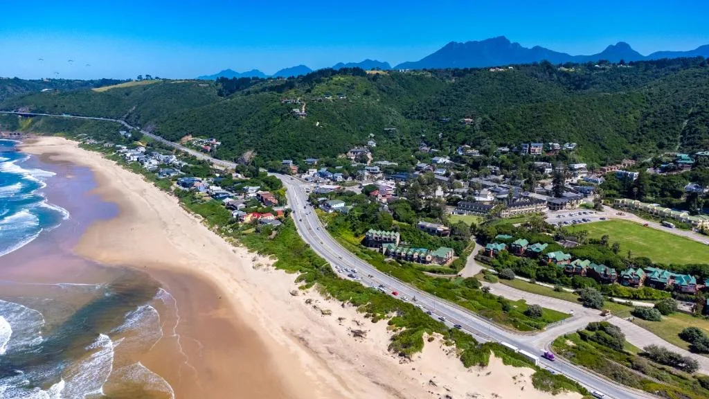 Aerial view of Wilderness beach with mountains, town, and coastal road