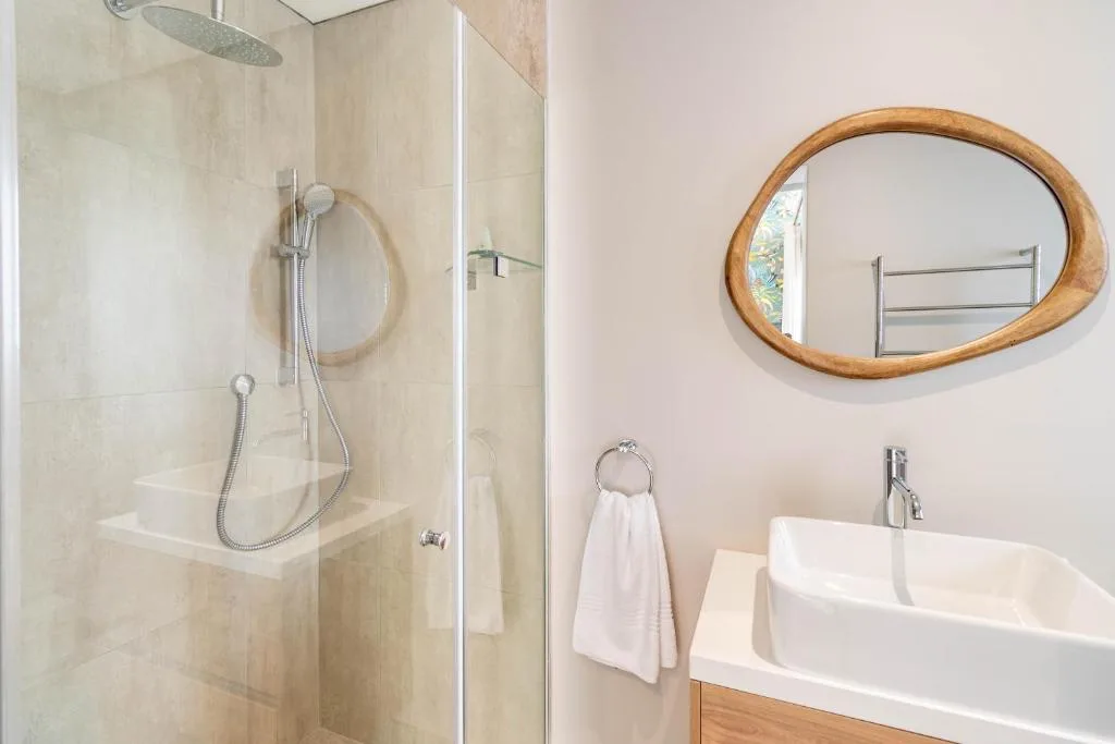 Modern bathroom with glass shower enclosure and oval wooden mirror