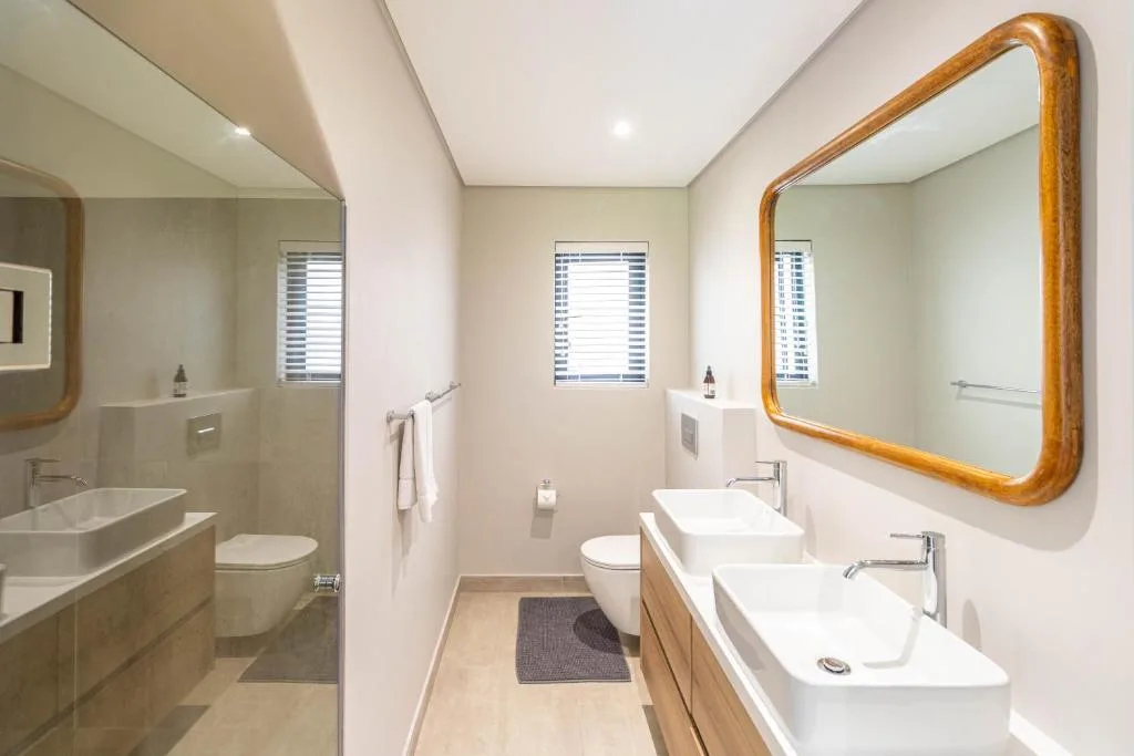 Modern bathroom with dual vanities, wooden mirror frame, walk-in shower