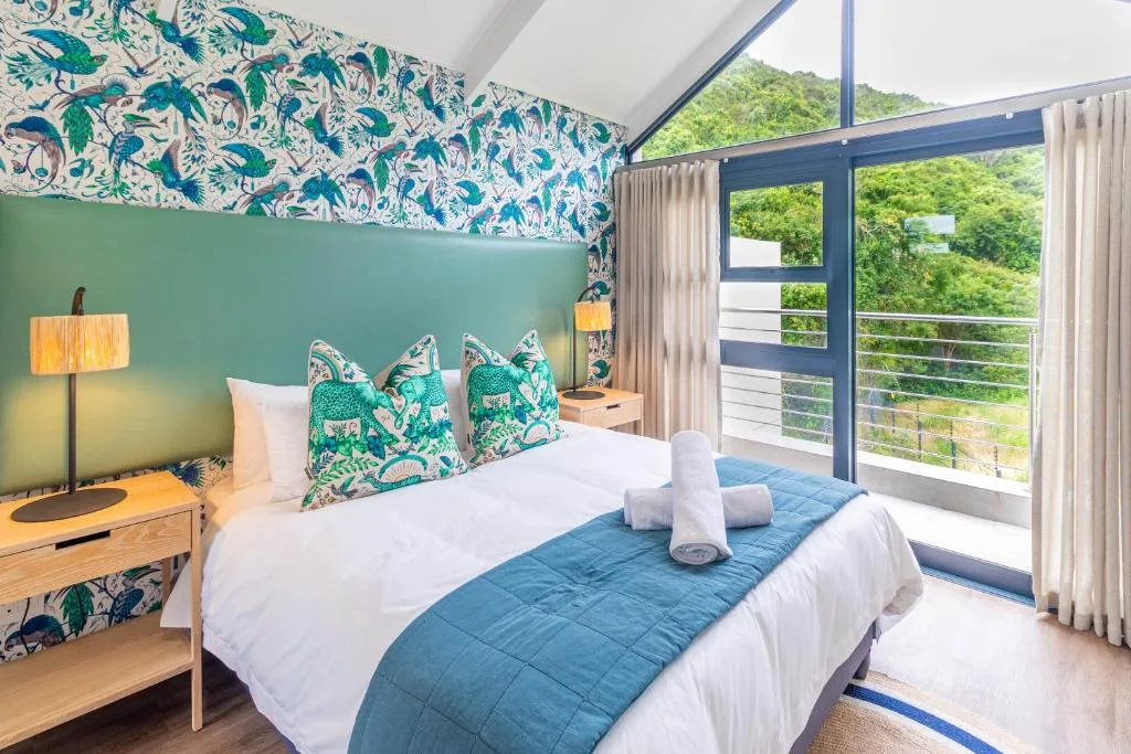 Bright bedroom with patterned wallpaper, green headboard, and mountain views through glass doors