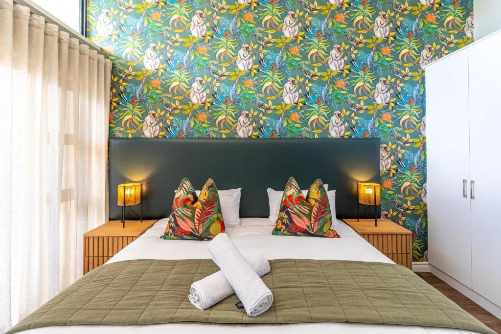 Modern bedroom with vibrant tropical wallpaper, colorful cushions, and contemporary lighting