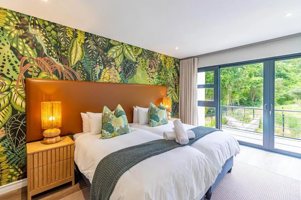 Modern bedroom with twin beds, vibrant botanical wallpaper, and forest views