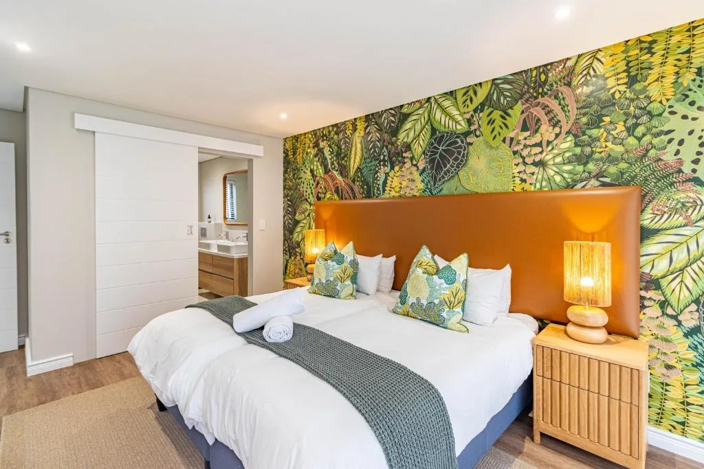 Modern bedroom with dual beds, vibrant botanical wallpaper, orange headboard, ensuite bathroom