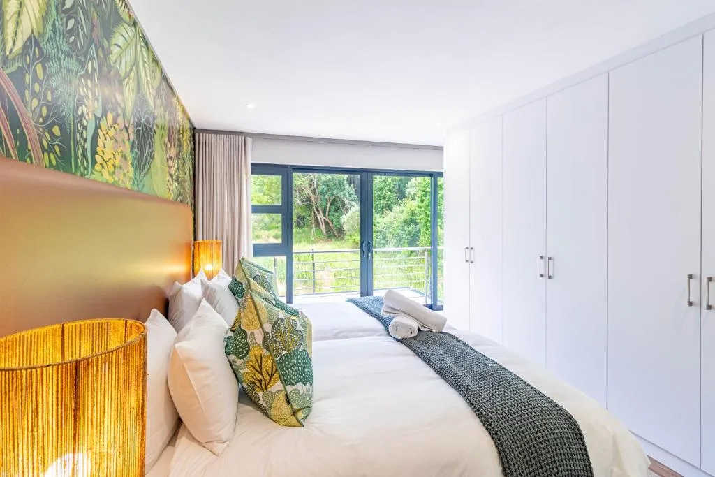 Modern bedroom with queen bed, botanical artwork, and garden views through glass doors