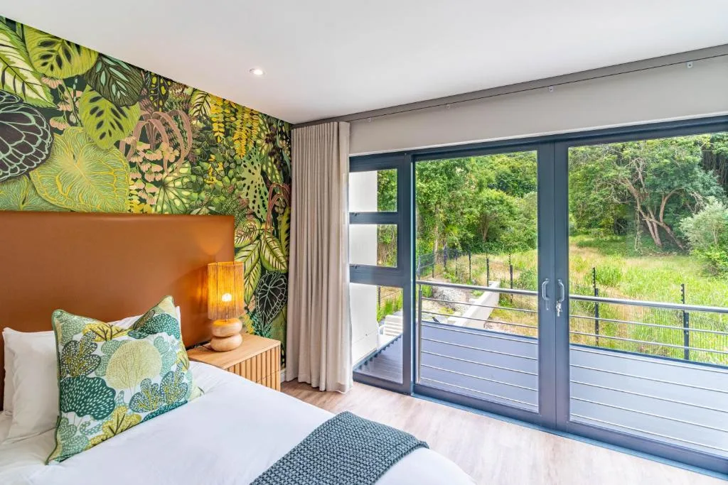 Modern bedroom with botanical wallpaper, orange headboard, garden views through glass doors