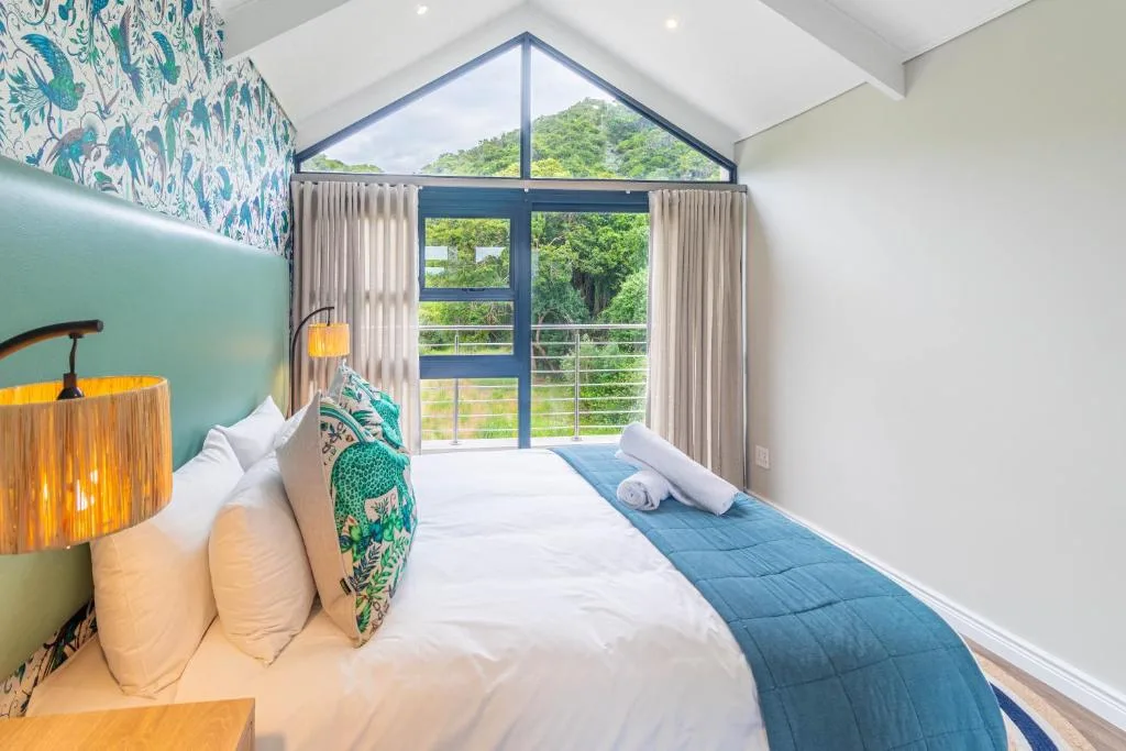 Modern bedroom with queen bed, feature wallpaper, large windows overlooking green landscape