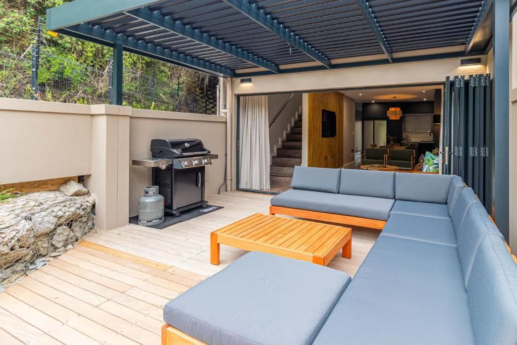 Modern outdoor patio with lounge seating, braai grill, and pergola shade structure