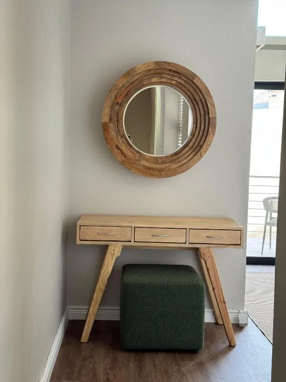 Wooden round mirror above desk with green upholstered stool accent