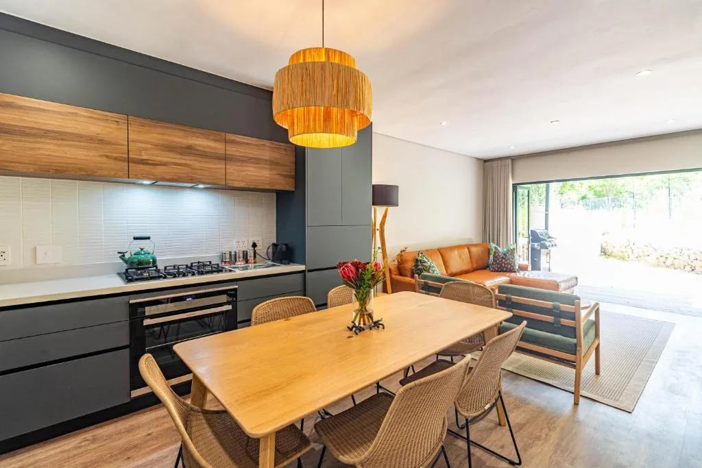 Modern dining table with woven chairs, kitchen and lounge visible beyond