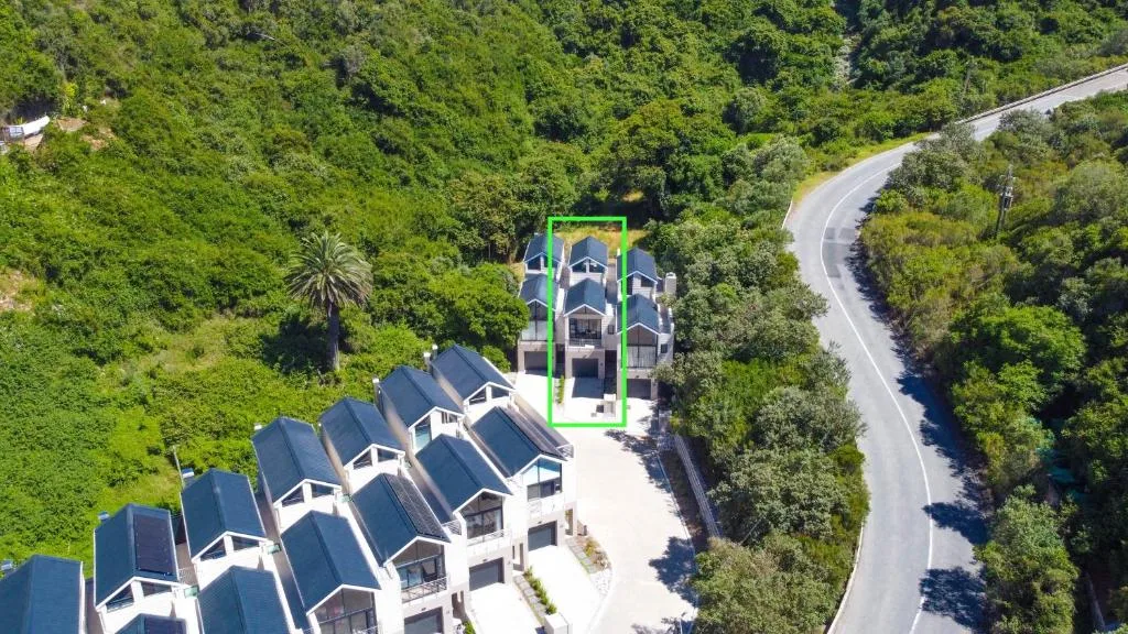 Aerial view of modern apartment complex nestled in lush green forest with winding road
