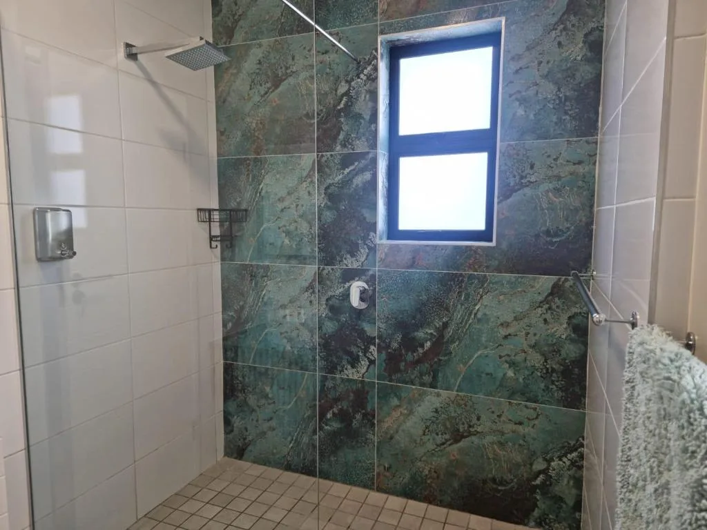 Modern bathroom with walk-in shower, green marble tiles, and natural light from window