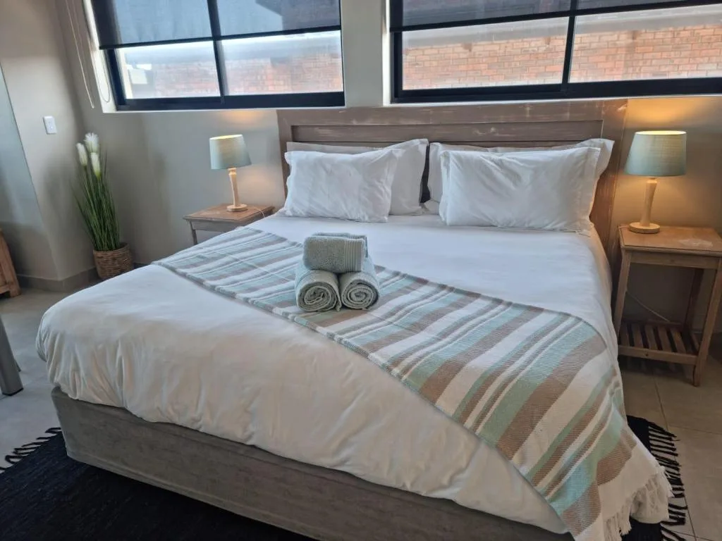 Neatly made bed with white linens, striped runner, and rolled towels