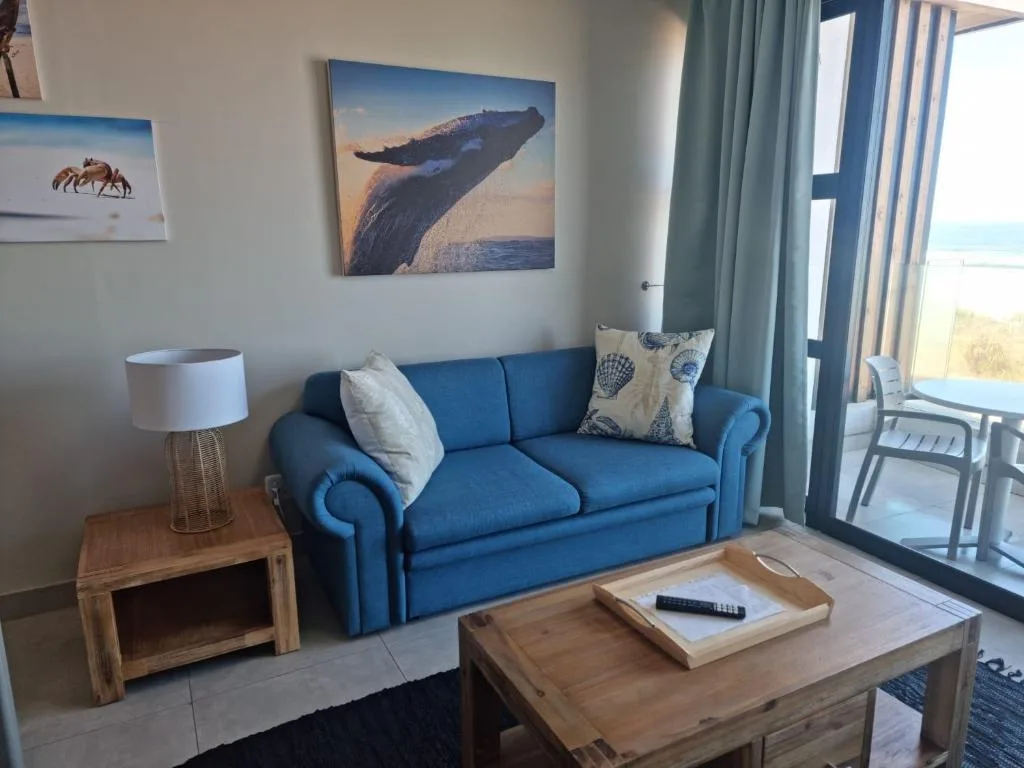 Bright lounge with blue sofa, ocean artwork, and coastal view through glass doors