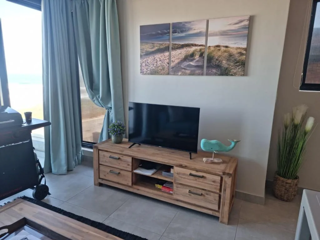 Modern lounge with TV, wooden cabinet, beach artwork, and ocean view through large windows