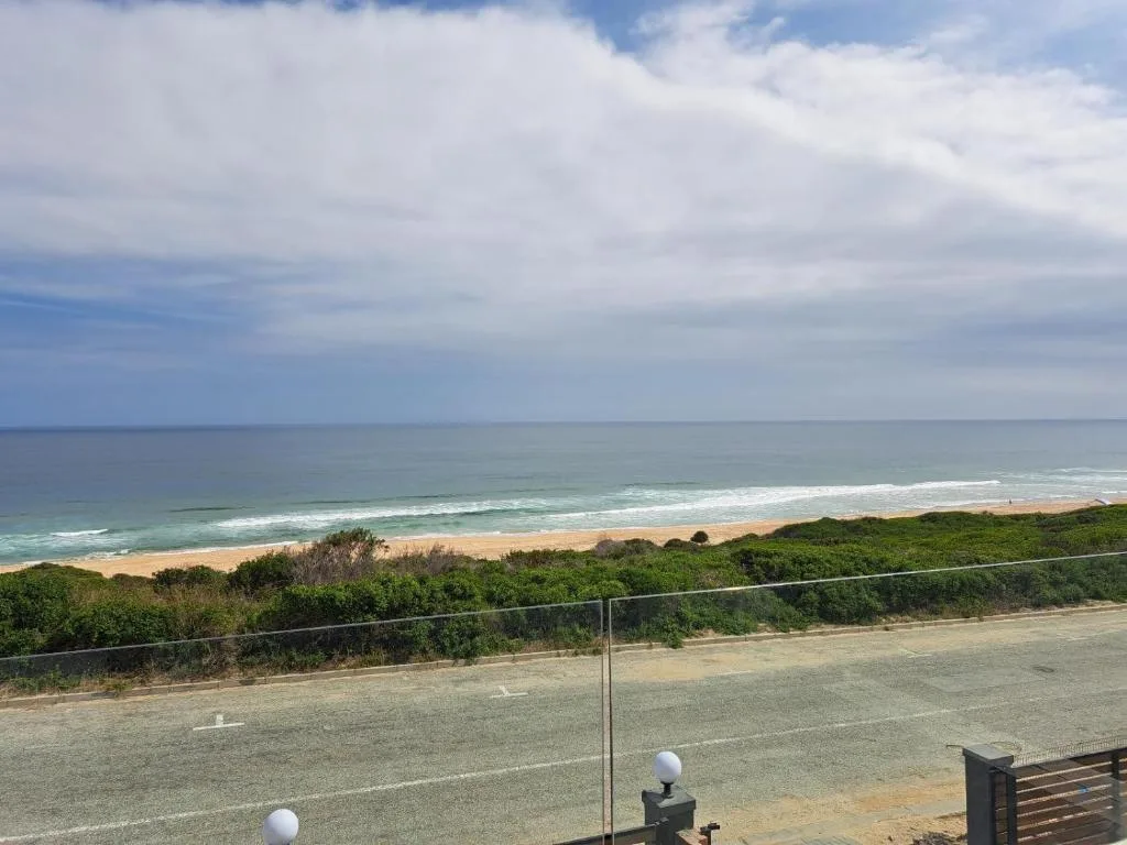 Expansive ocean and beach vista with golden sand and green coastal vegetation
