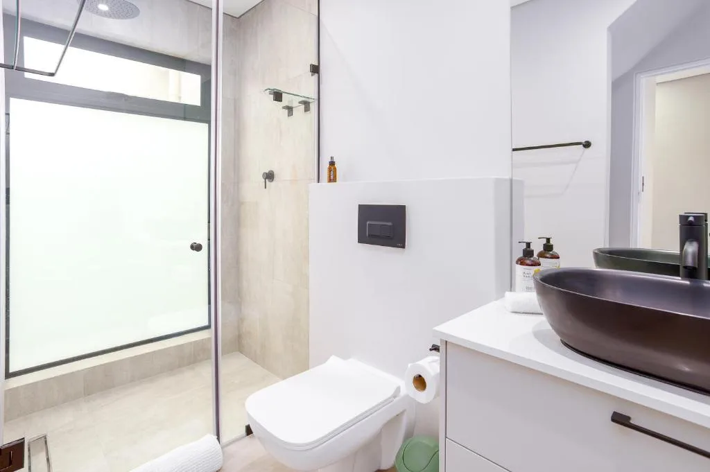 Modern bathroom with dark vessel sink, glass shower enclosure, white toilet
