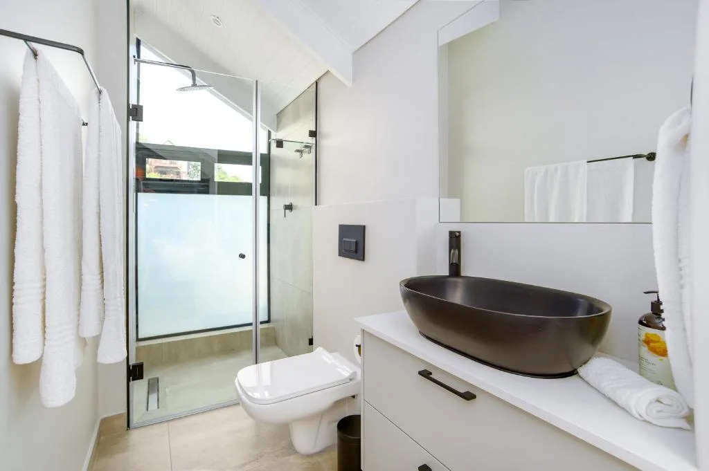 Modern bathroom with black oval basin, glass shower enclosure, and white towels