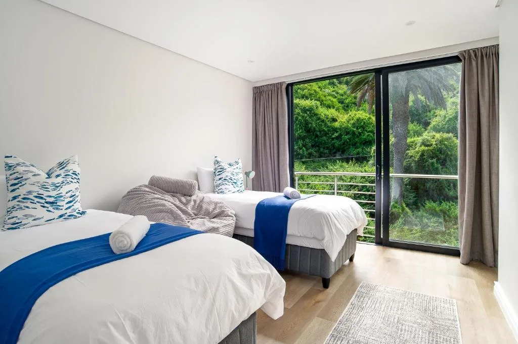 Bright bedroom with two beds and views of lush green forest landscape