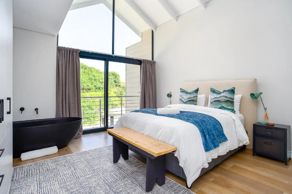 Modern bedroom with queen bed, en-suite bathtub, and glass doors opening to balcony views