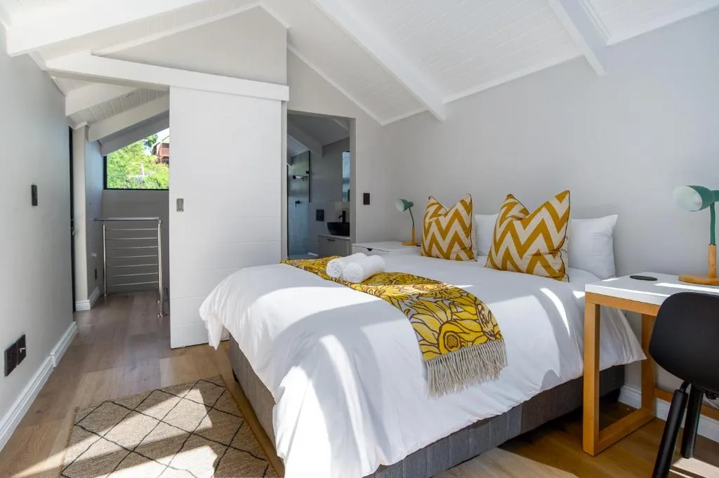 Bright modern bedroom with twin beds, yellow patterned pillows, vaulted ceiling