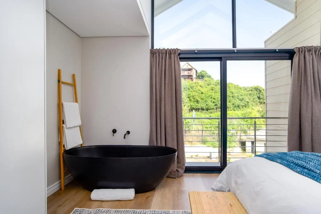 Bedroom with standalone black bath tub and garden views through glass doors
