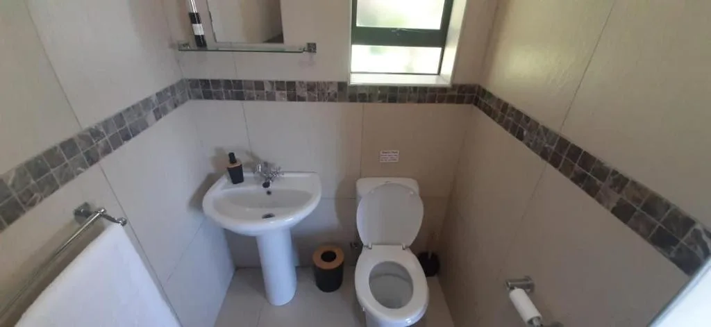 Clean bathroom with pedestal sink, toilet, and tiled walls with window
