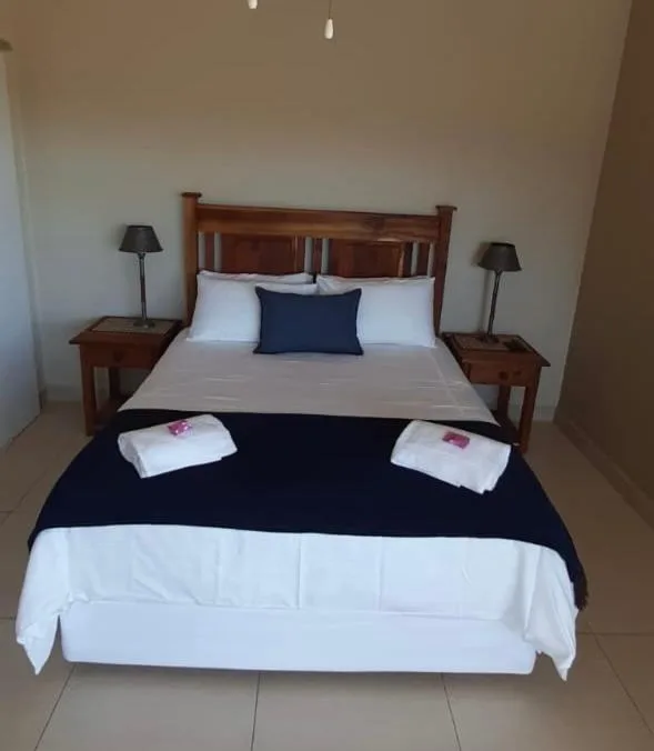 Wooden bed with white pillows and navy bedding, matching bedside tables with lamps