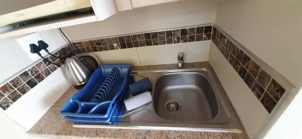 Compact kitchen sink with dish rack and kettle on counter