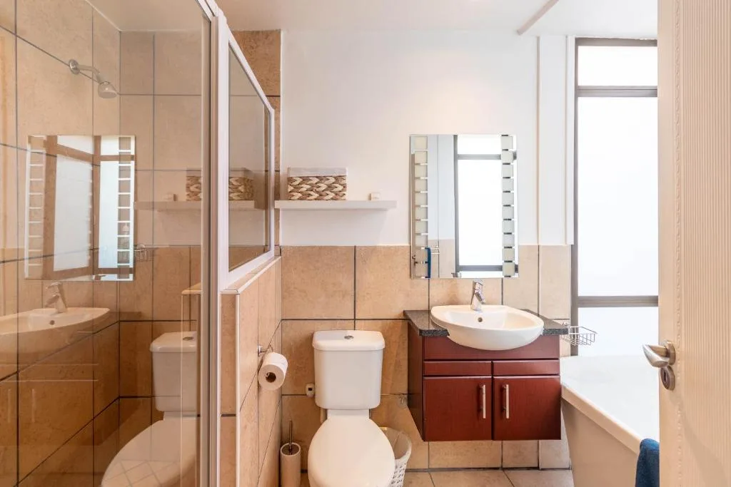 Modern bathroom with shower, toilet, and dual sinks with red cabinetry