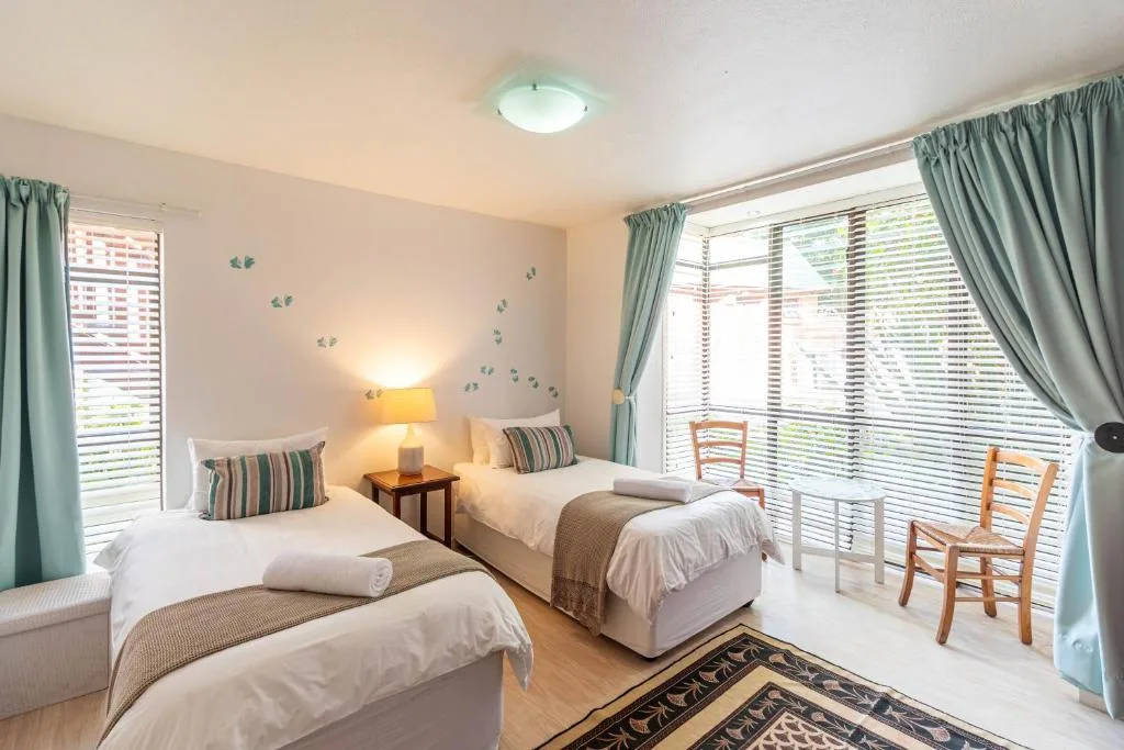Bright bedroom with two twin beds, wooden chairs, and louvred windows