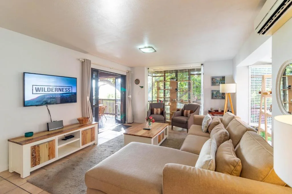 Bright lounge with cream sofas, TV, and deck access overlooking garden