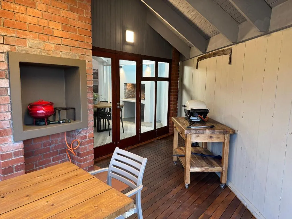 Outdoor deck with wooden table, braai grill, and covered seating area