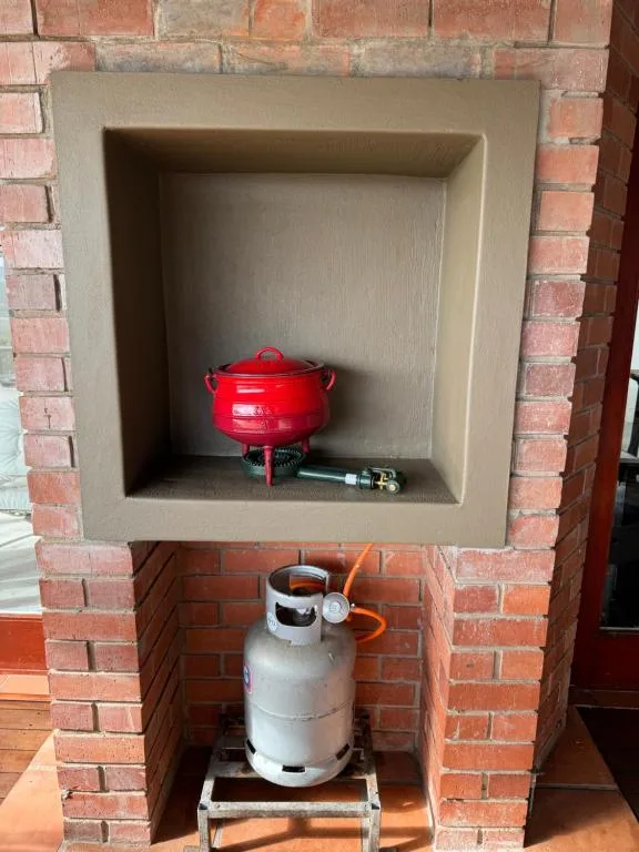 Red braai pot and gas cylinder built into brick fireplace niche