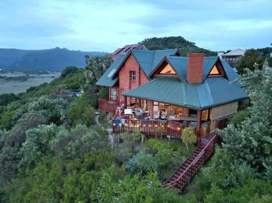 Red brick house with blue metal roof overlooking Wilderness lagoon and mountains