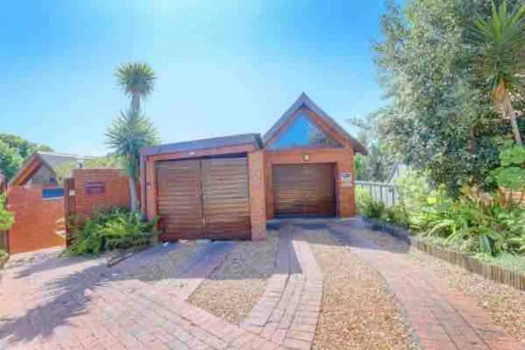 Red brick garage and entrance with palm trees and lush gardens surrounding