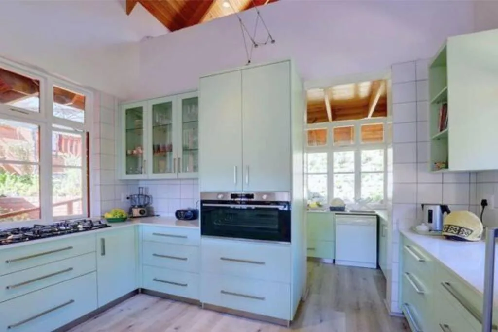 Bright kitchen with pale green cabinetry, gas stove, and garden views