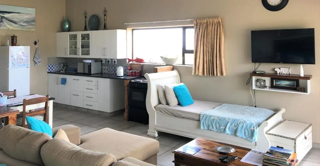 Open-plan lounge with cream sofa, TV, and kitchen visible in background