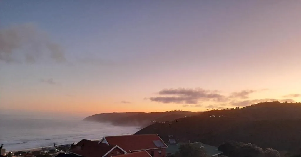Scenic sunset over ocean with forested cliffs and coastal homes below