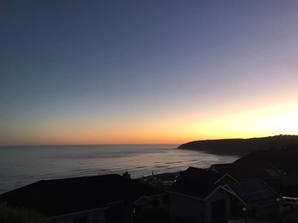 Sunset over ocean with coastal cliffs and property rooflines below